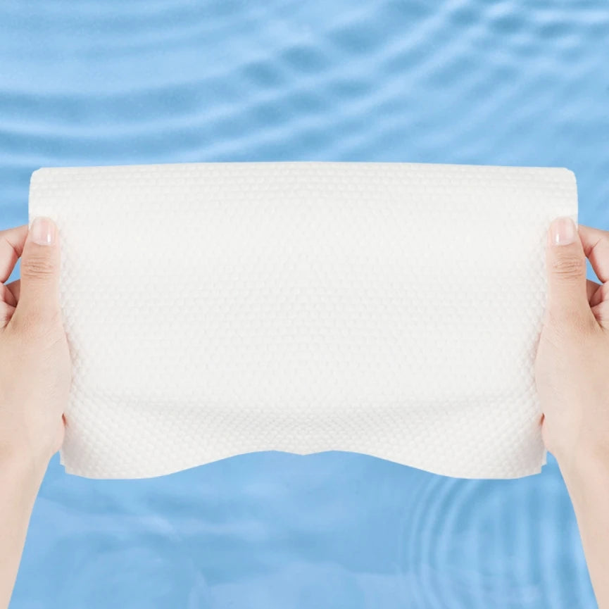 Hands holding a white, textured facial cleansing towel against a light blue water background.