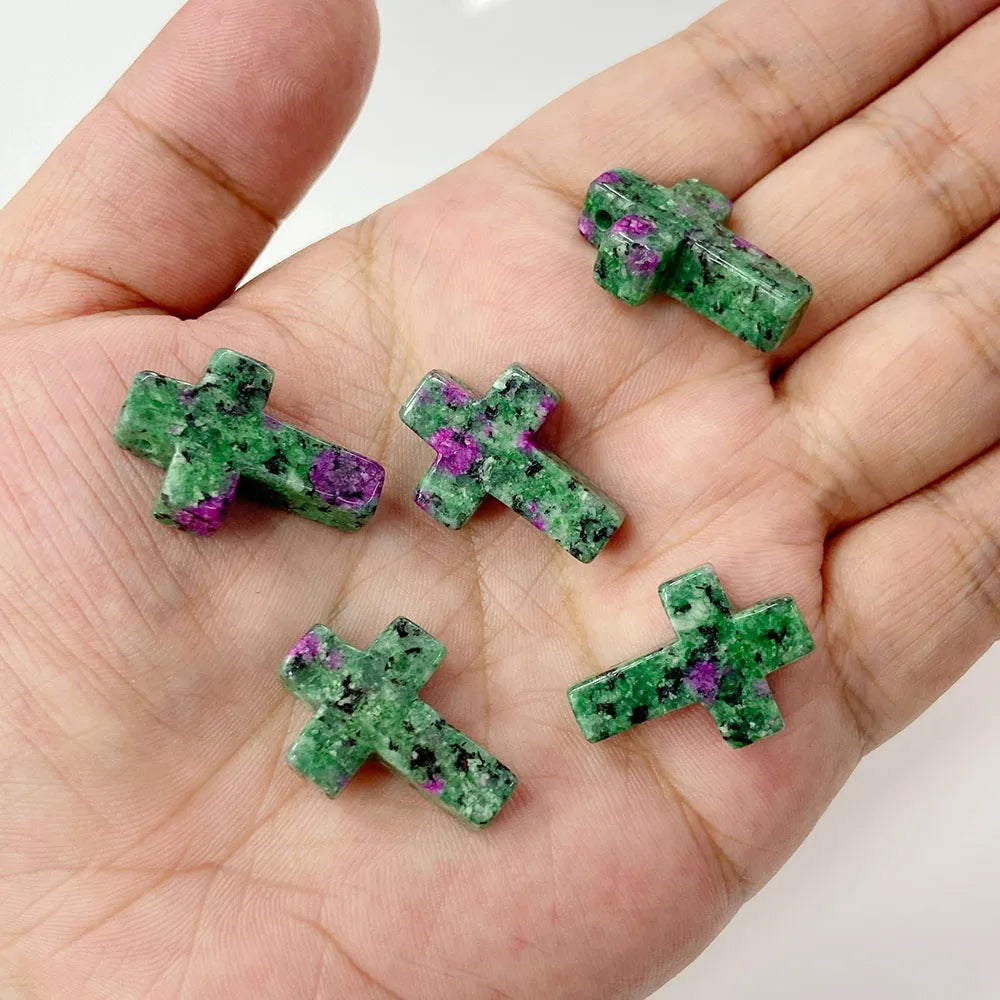 A hand holds several green and purple natural agate and jasper cross pendant charms.