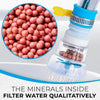 Klares Plastik-Wasserfilterflasche mit gelbem Deckel und Sieb, neben einem Haufen rosa kugelförmiger Filterperlen.