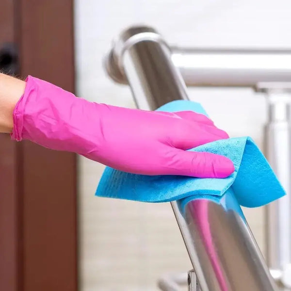 A hand wearing a bright pink disposable nitrile cleaning glove is wiping down a stainless steel fixture.