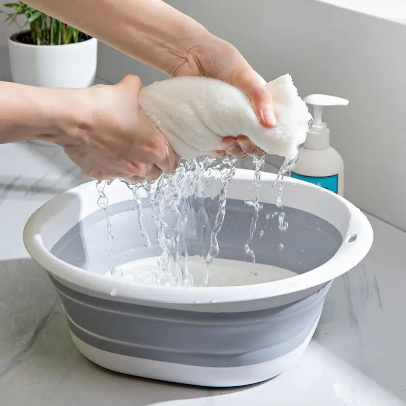 A hand is pouring water over a white, fluffy cloth into a gray plastic wash basin.
