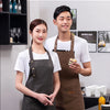 A young couple wearing dark canvas aprons standing in a modern kitchen setting.