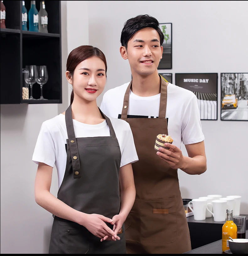 A young couple wearing dark canvas aprons standing in a modern kitchen setting.