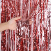 Eine Hand hält und manipuliert vertikale Stränge aus metallischem rosa Glitzer-Folie-Flimmer-Hintergrundvorhänge.