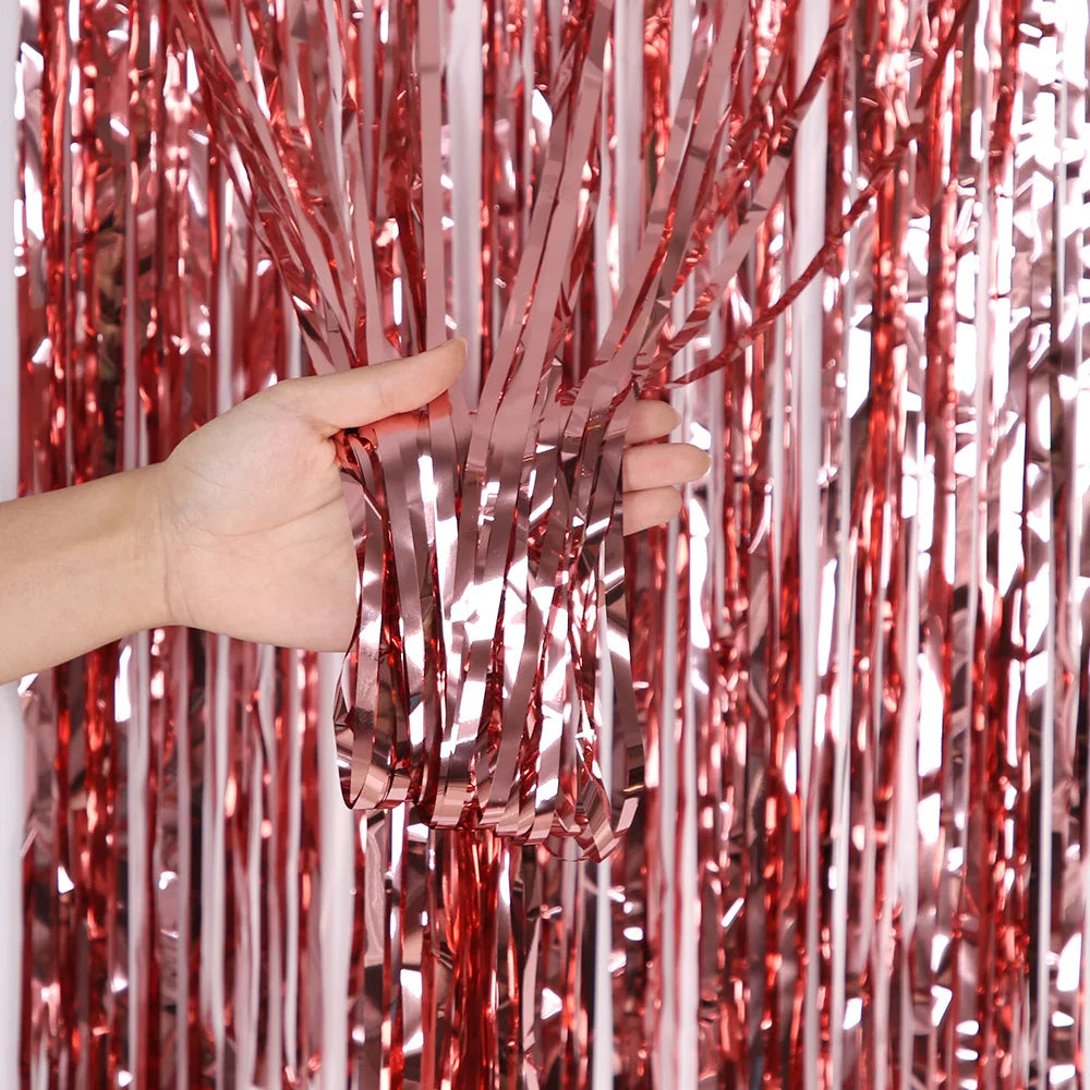 Eine Hand hält und manipuliert vertikale Stränge aus metallischem rosa Glitzer-Folie-Flimmer-Hintergrundvorhänge.