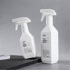 A white refillable plastic spray bottle with a pump dispenser is shown against a gray background.