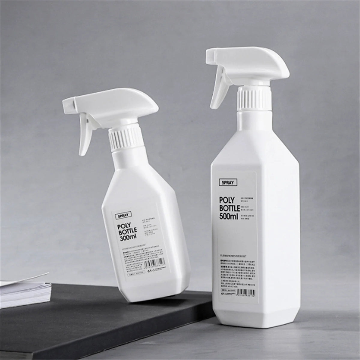 A white refillable plastic spray bottle with a pump dispenser is shown against a gray background.
