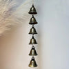 A vertical arrangement of small, antique bronze metal wind chimes hanging from a feathery plume.