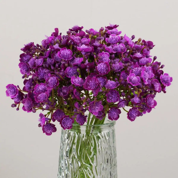 A bouquet of purple artificial baby's breath flowers in a clear glass vase.