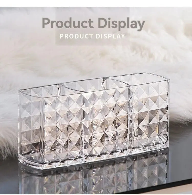 Clear acrylic makeup brush holder with three compartments displayed on a reflective surface.