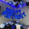 A display of blue and black balloons spelling out Happy Birthday on a gray wall.
