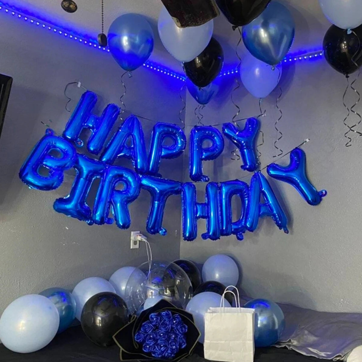 A display of blue and black balloons spelling out Happy Birthday on a gray wall.