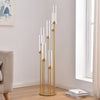 Centro de mesa de candelabro de 7 brazos dorado y alto con velas de vidrio transparente en una pared blanca.