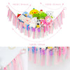 A colorful bohemian stuffed animal hammock featuring various plush toys hanging from pink and purple streamers.
