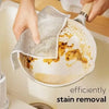 Hands are using a mesh cleaning cloth to remove stains from a non-stick pan.