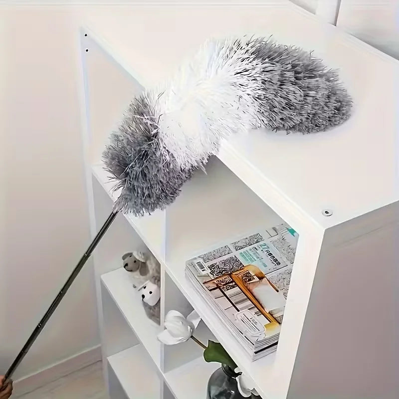 A gray and white fluffy microfiber duster with an extension rod is displayed on a white shelf.