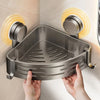 A hand is holding a triangular stainless steel suction cup storage shelf against a light-colored wall.