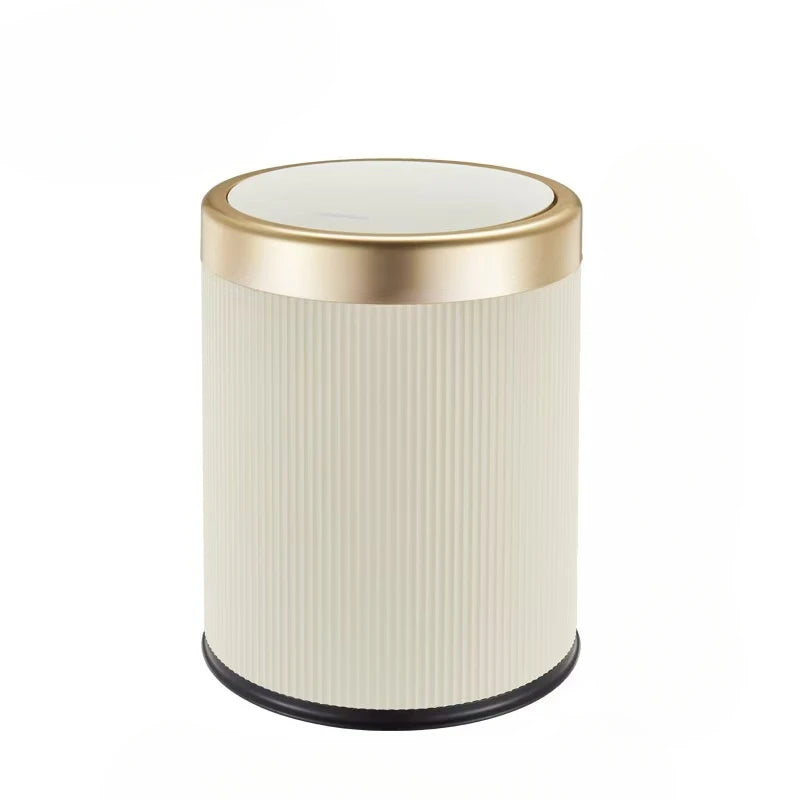 A cylindrical trash can with a gold rim and off-white ribbed body.
