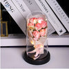Ein Glasstrauß rosa Rosen und getrockneter Blumen in einer klaren Glasvase auf einer schwarzen Basis.