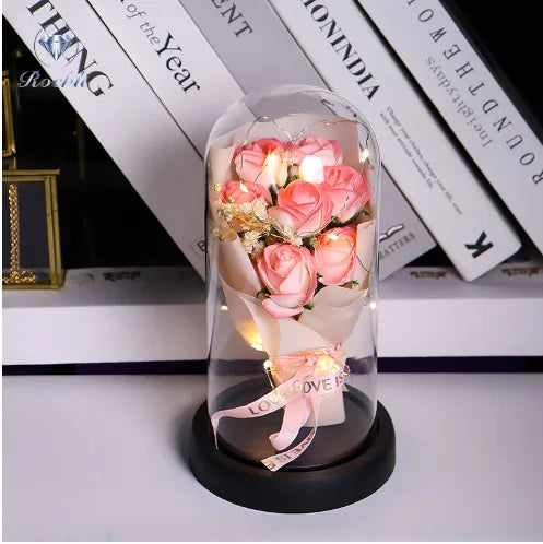Ein Glasstrauß rosa Rosen und getrockneter Blumen in einer klaren Glasvase auf einer schwarzen Basis.