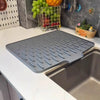 A gray silicone drain mat is placed inside a stainless steel kitchen sink basin.