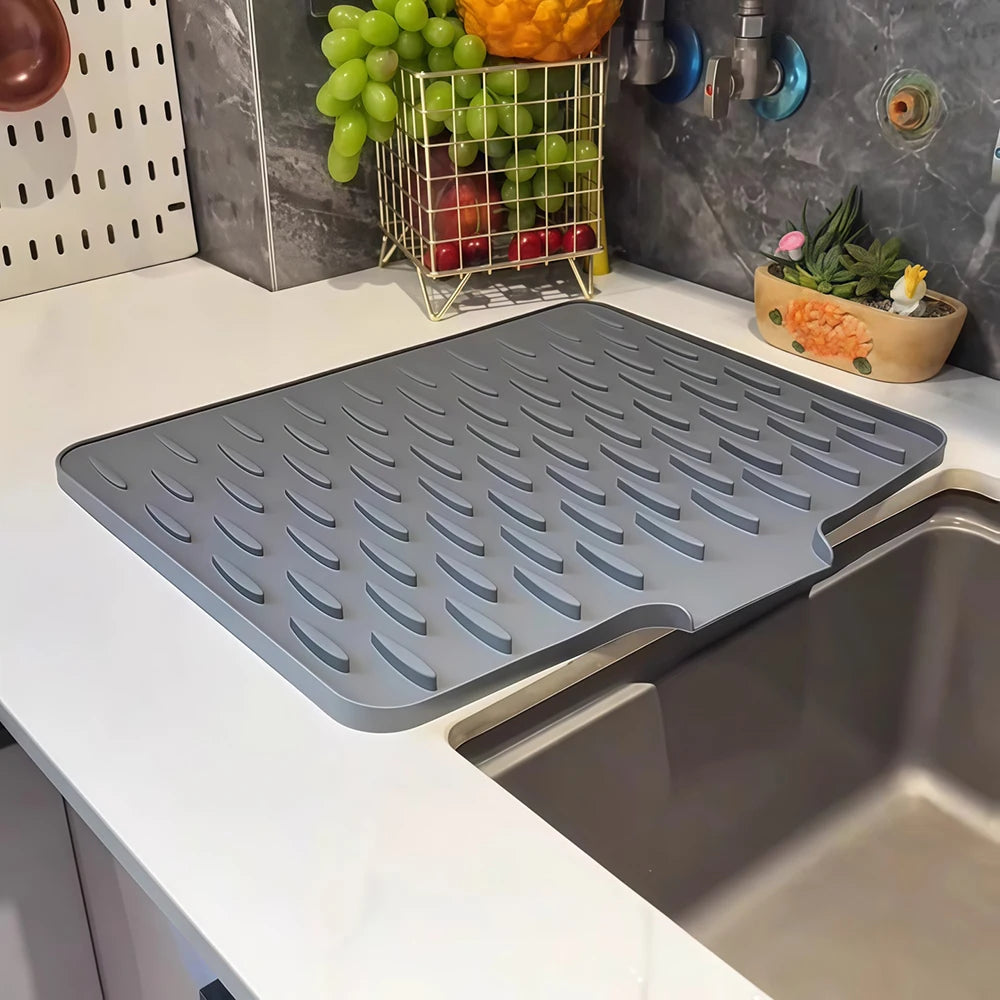 A gray silicone drain mat is placed inside a stainless steel kitchen sink basin.