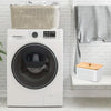 A white washing machine is shown next to a woven basket and a gray towel hanging on a white brick wall.