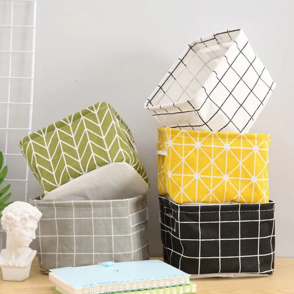 A stack of cotton and hemp storage baskets in various shades of gray, black, and yellow, with a light blue book underneath.