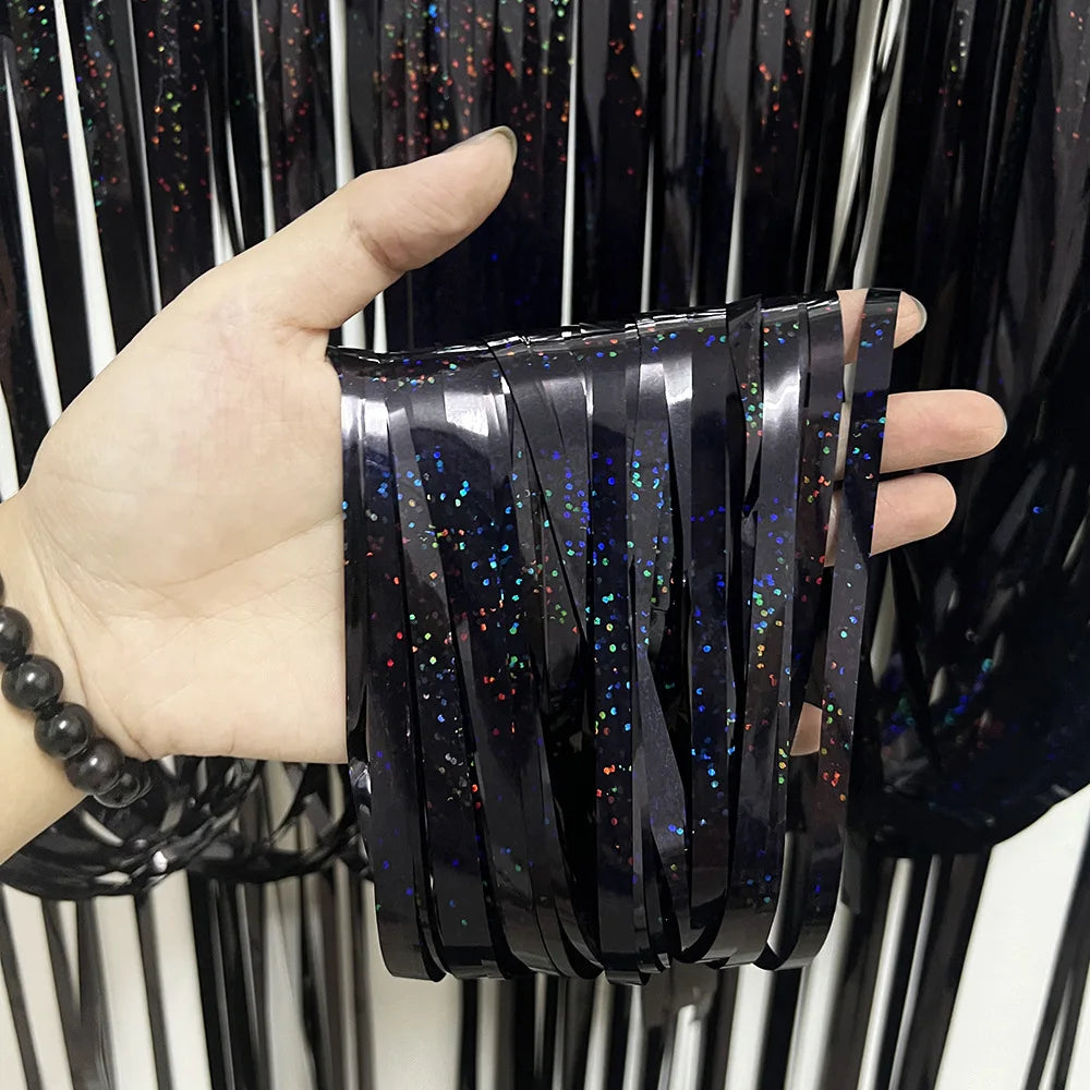 Eine Hand hält einen Bund schwarzer metallischer Tinselfolie-Vorhänge mit irisierendem Glitzer.
