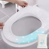 A hand is placing a disposable white toilet seat onto a white toilet bowl.