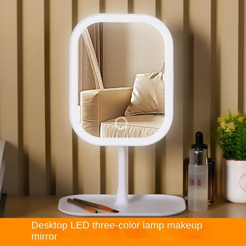 A white LED desktop mirror with a round frame reflects a person in a neutral-toned room.