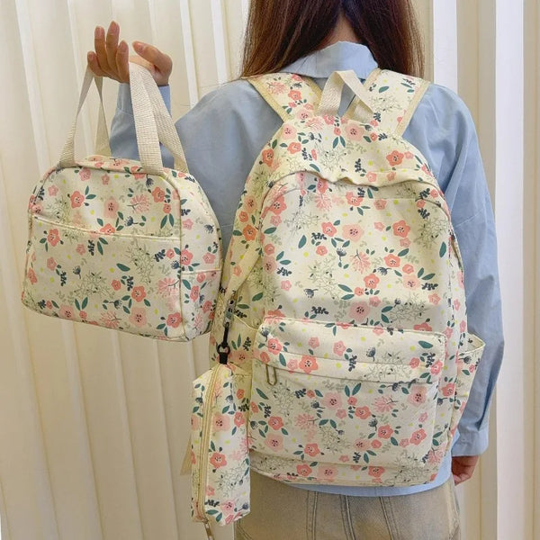 A person is holding a floral print backpack, a matching handbag, and a pencil case against a light background.