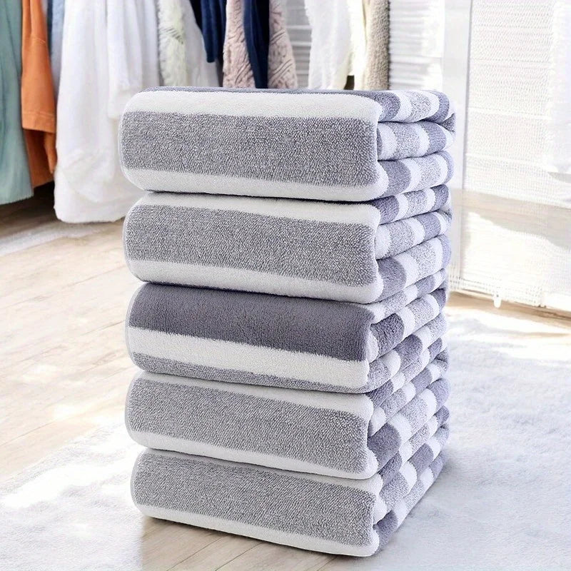 A stack of gray and white striped microfiber bath towels on a light floor.