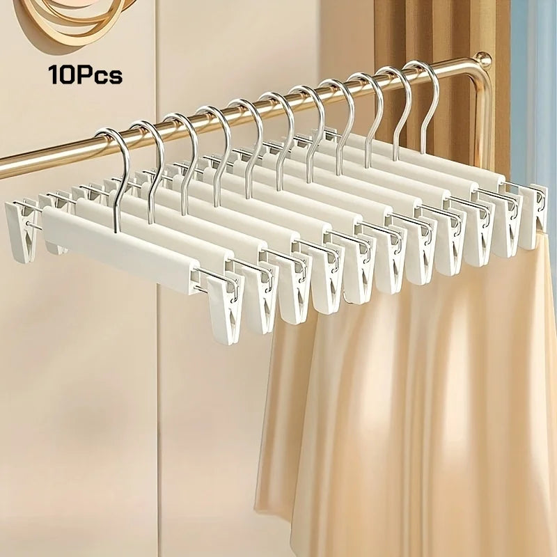 A set of 10 white adjustable clothes hangers hanging on a gold-colored rod.
