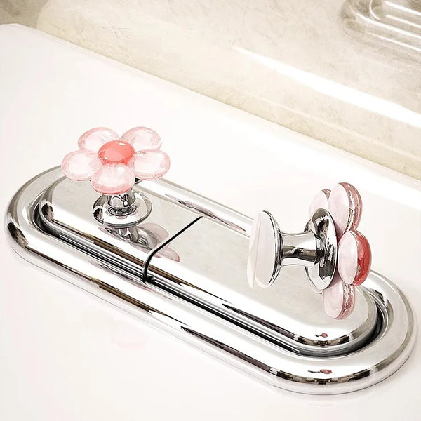 A chrome toilet flush button set featuring pink and white decorative flower shaped flush buttons.