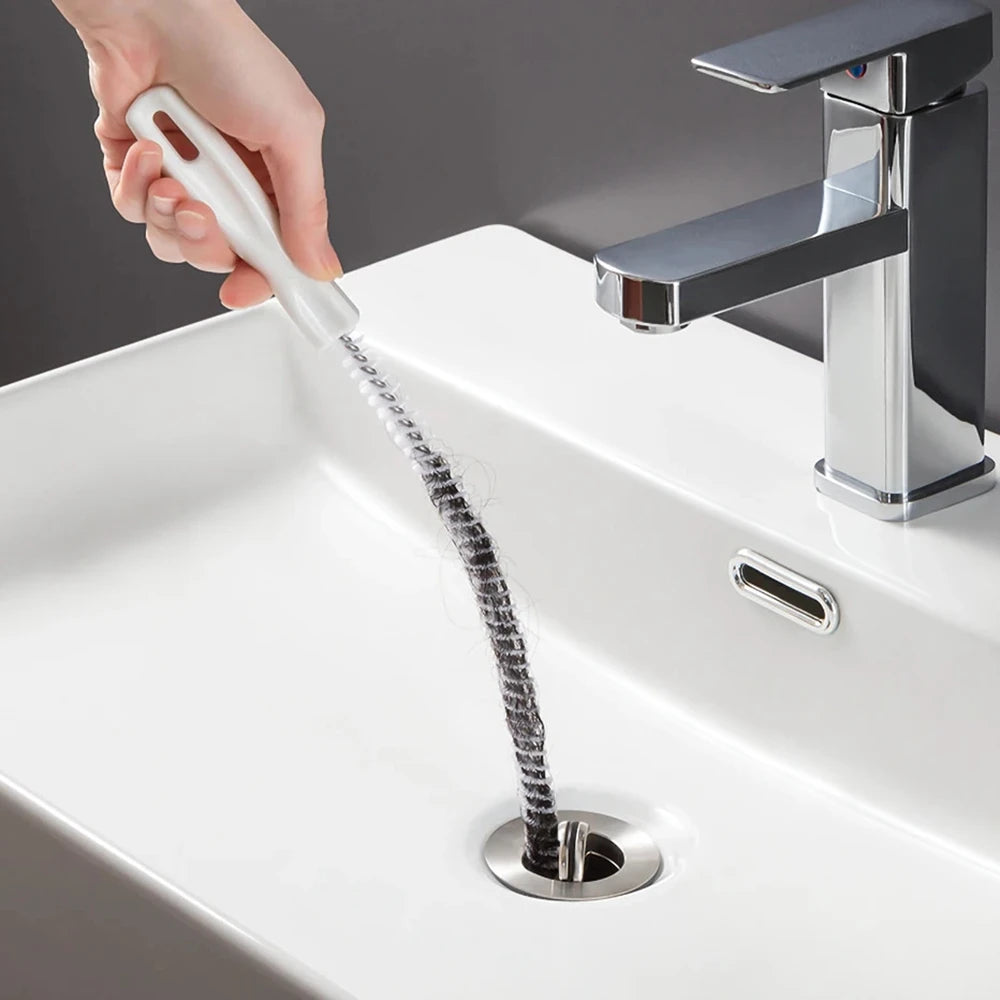 A hand is using a flexible drain cleaning brush to clear a sink drain.