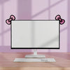 Un moniteur d'ordinateur avec une base blanche et un clavier sur un bureau en bois, encadré par des décorations en nœuds rose
