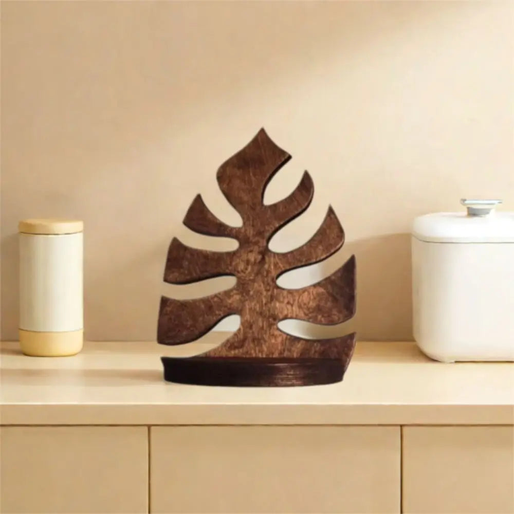 A dark brown wooden leaf wall art frame displayed on a light wood shelf next to white ceramic containers.