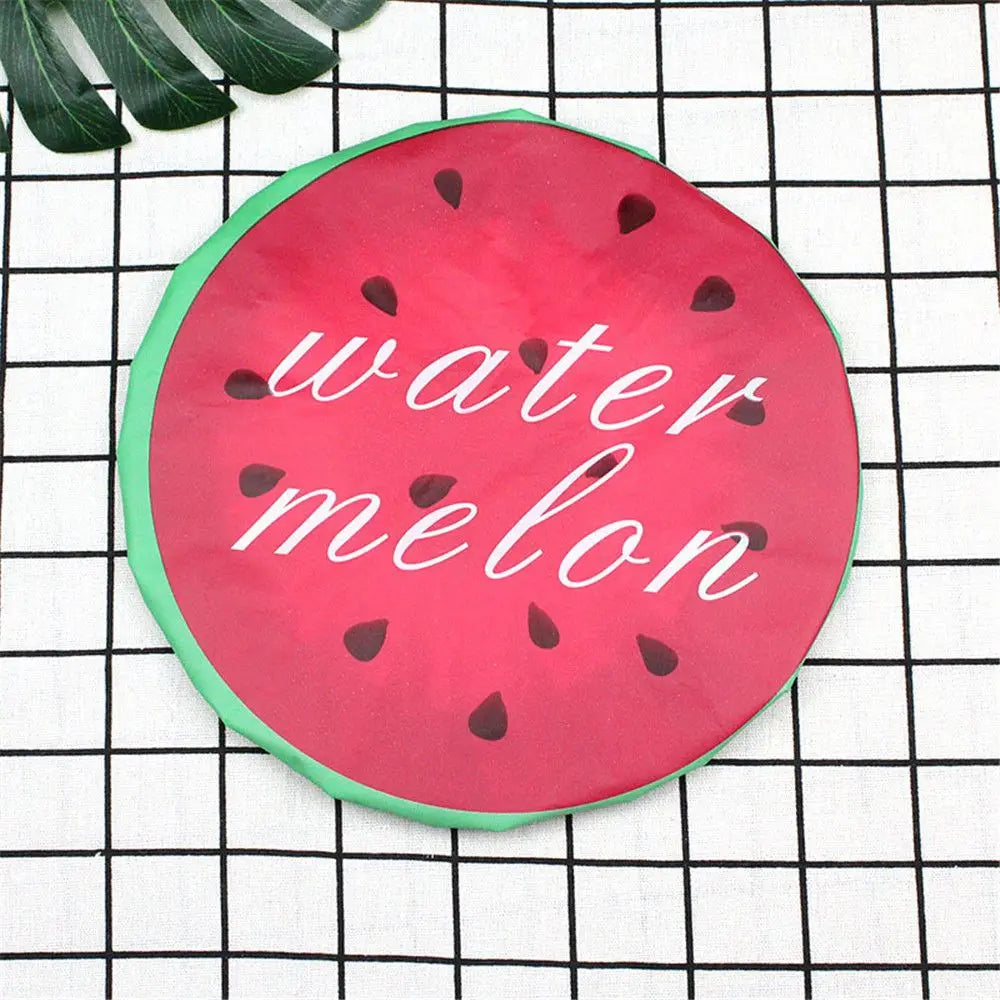 A bright pink watermelon-shaped reusable fruit shower cap rests on a black and white checkered cloth.