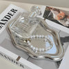 A glass perfume bottle and a pearl necklace are displayed in a silver jewelry organizer tray.