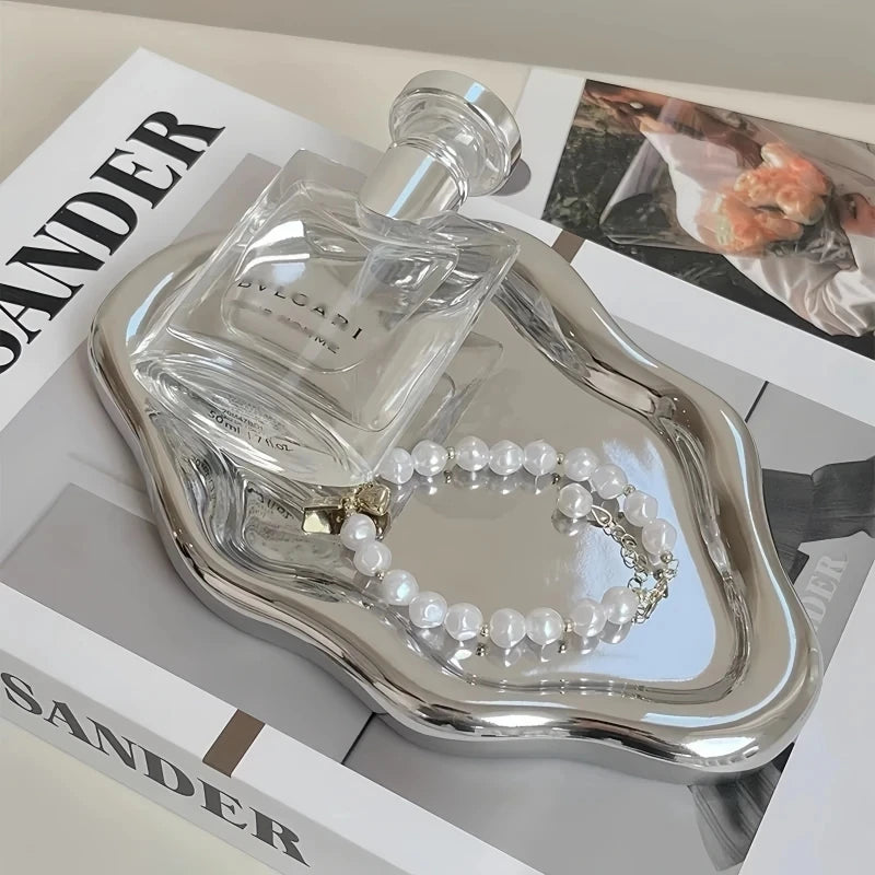 A glass perfume bottle and a pearl necklace are displayed in a silver jewelry organizer tray.