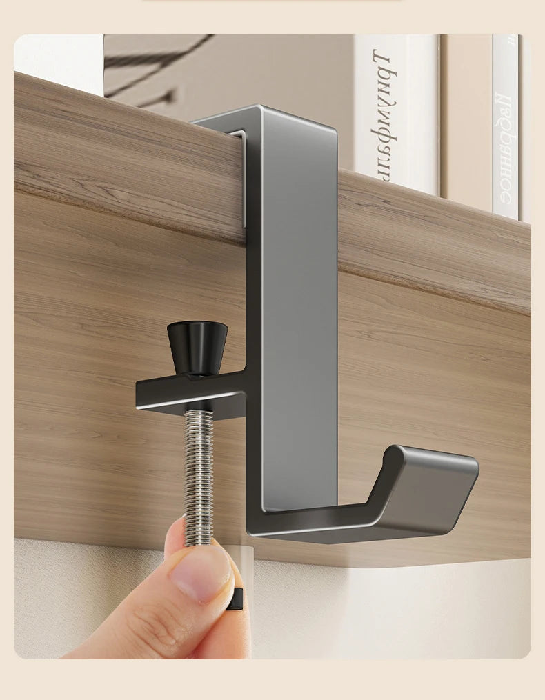 A close-up of a silver aluminum desk hanging hook being installed on a wooden surface.