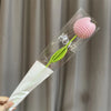 Bouquet de fleurs de carnation en coton fait main avec des éléments roses et verts, présenté dans une gaine en plastique tran