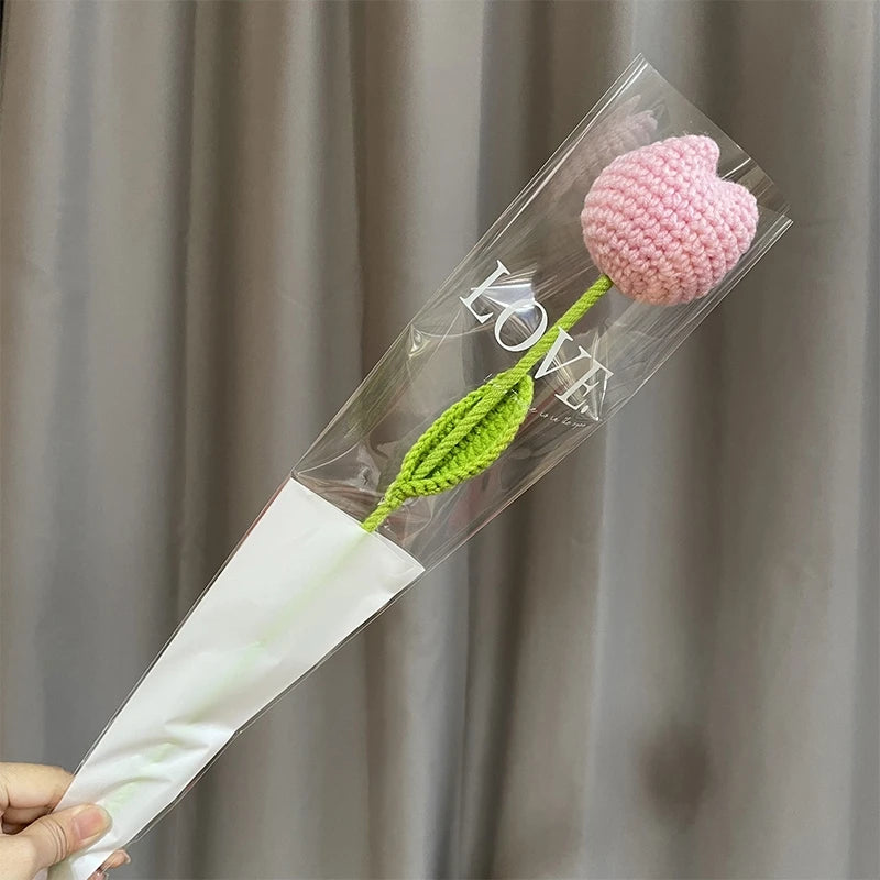 Bouquet de fleurs de carnation en coton fait main avec des éléments roses et verts, présenté dans une gaine en plastique tran