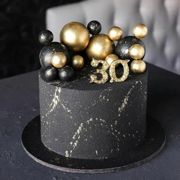 A black cake with gold and dark ball decorations and the number 30 on top