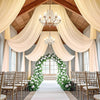 Elegant indoor event decor featuring sheer chiffon draping fabric and a white floral archway