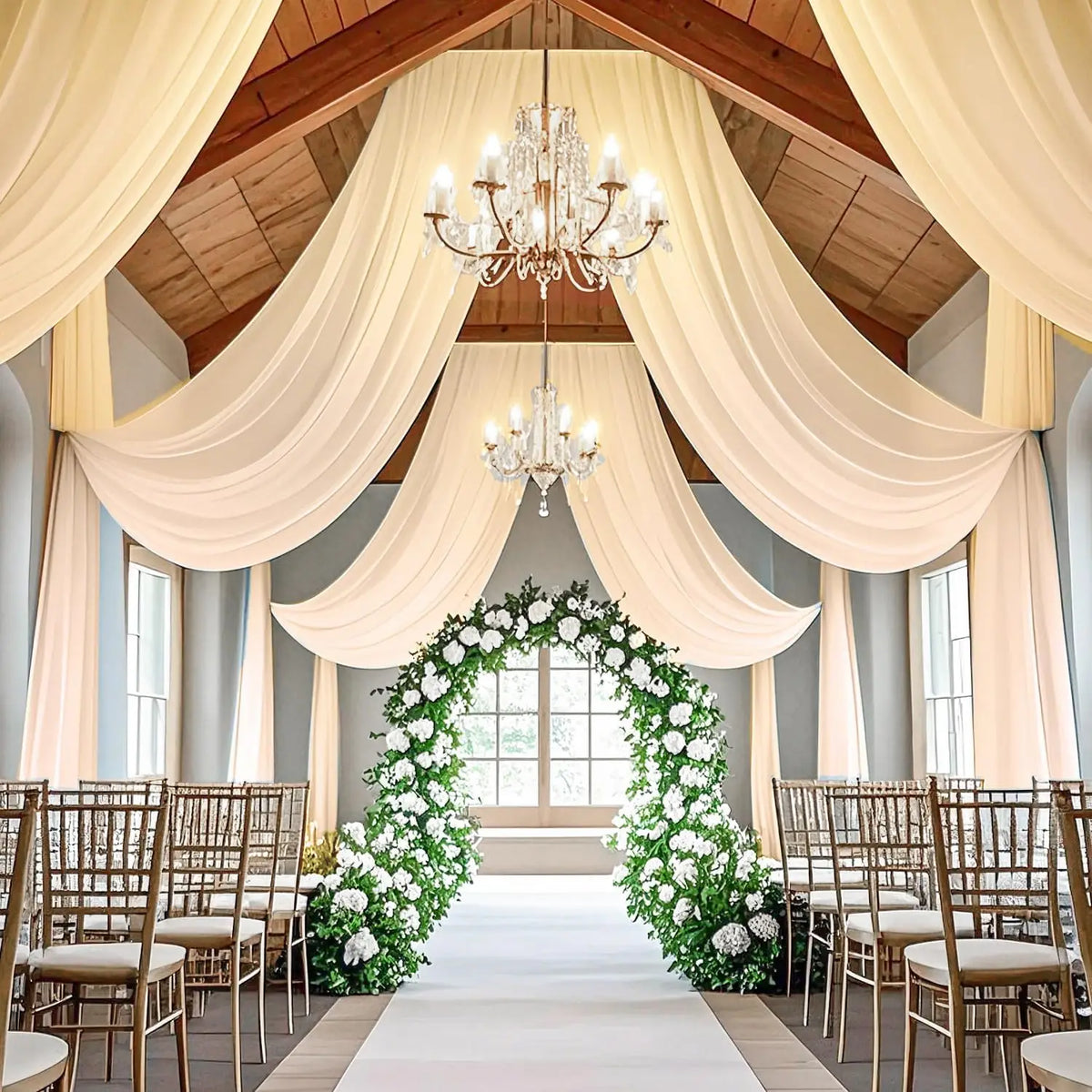 Elegant indoor event decor featuring sheer chiffon draping fabric and a white floral archway