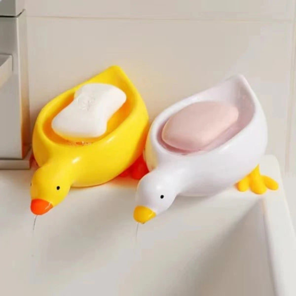 A yellow duck-shaped soap dish holding a white bar of soap on a white bathroom shelf.
