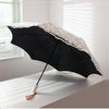 A black sun umbrella with white embroidered detailing is shown open on a white surface.
