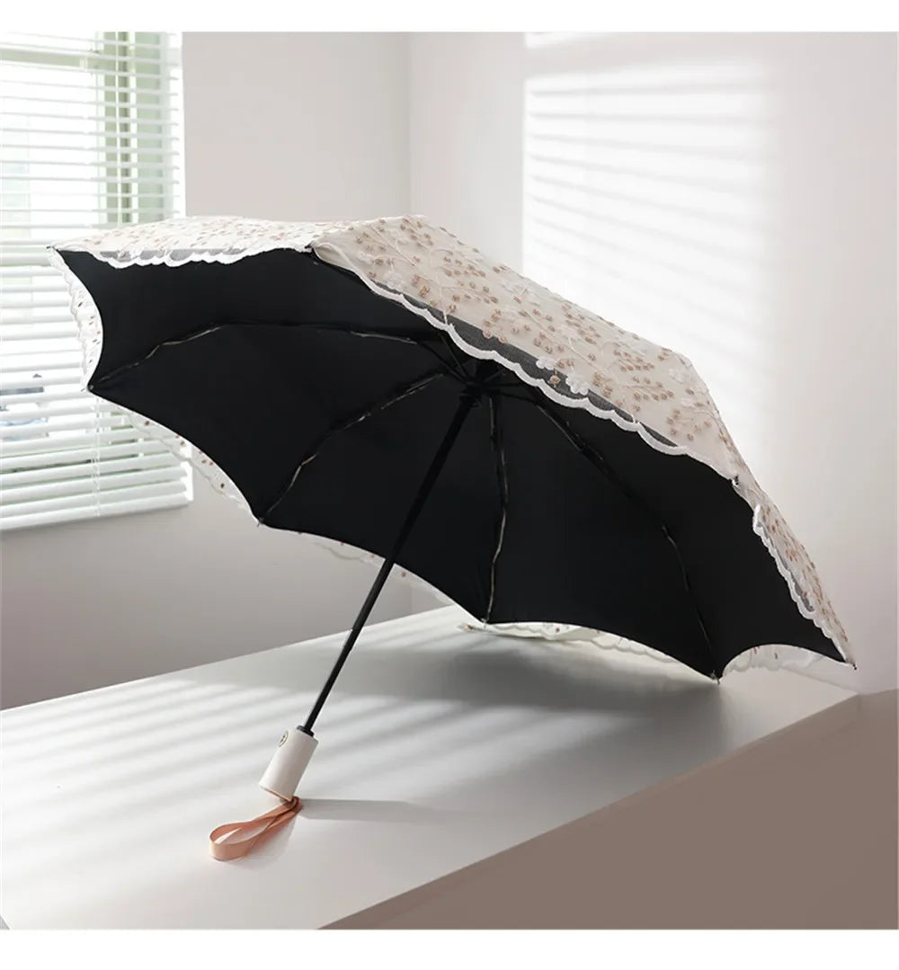 A black sun umbrella with white embroidered detailing is shown open on a white surface.
